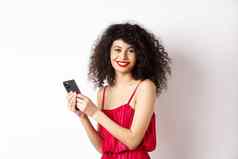 快乐优雅的女人红色的衣服写作消息智能手机微笑相机站白色背景