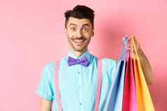 图像快乐的家伙购物持有纸袋微笑兴奋购物者购买折扣站粉红色的背景