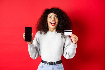 在线购物快乐年轻的女人显示塑料信贷卡空电话屏幕宣布促销提供站红色的背景