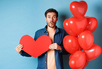情人节一天概念的男朋<strong>友爱</strong>惊讶相机持有红色的纸心站浪漫的气球蓝色的背景