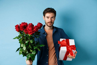 浪漫情人节一天男人。展示花束红色的玫瑰情人的男朋友带花礼物浪漫的日期站蓝色的背景