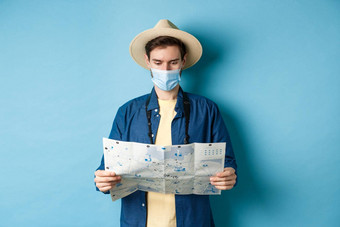 科维德流感大流行旅行概念年轻的男人。医疗面具阅读<strong>旅游地</strong>图搜索路线观光景点站蓝色的背景