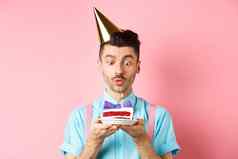 假期庆祝活动概念快乐年轻的男人。生日聚会，派对他吹蜡烛蛋糕使生日站粉红色的背景