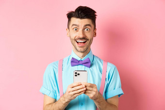 在线购物快乐男人。惊讶阅读智能手机屏幕微笑兴奋相机站粉红色的背景