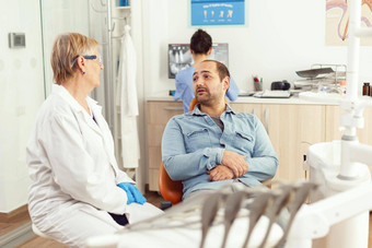 专家高级牙医讨论男人。病人坐着牙科椅子