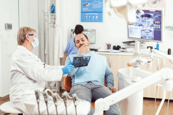 高级女人牙医检查牙射线照相法生病的男人。