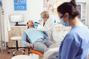高级口腔学家持有消毒牙科工具会说话的生病的病人