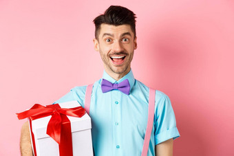 假期庆祝活动概念快乐年轻的男人。节日装持有大现在盒子生日站快乐的微笑粉红色的背景