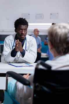 年轻的黑色的医生会说话的无效的病人办公室桌子上