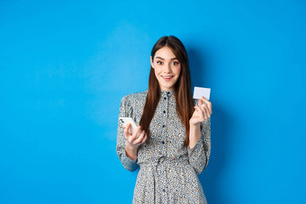 在线购物美丽的女人支付订单智能手机塑料信贷卡微笑相机穿衣服蓝色的背景