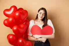 浪漫的女人拥抱大红色的心微笑梦幻下降爱情人节一天做梦情人站米色背景气球