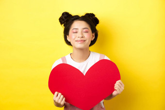 可爱的十几岁的亚洲女孩做梦真正的爱关闭眼睛显示大红色的心断路等待灵魂伴侣情人节一天站浪漫的化妆黄色的背景