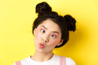 关闭肖像有趣的亚洲青少年女孩魅力化妆发型眯着眼看眼睛皱纹嘴唇愚蠢的站黄色的背景