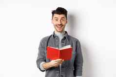爱好休闲快乐年轻的男人。阅读规划师持有日记红色的杂志微笑使笔记站白色背景