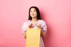 美丽的亚洲女孩做梦持有购物袋站粉红色的背景