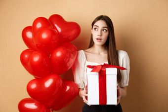 情人节一天沉思的可爱的女孩猜测使礼物持有现在好奇的上左角落里站浪漫的心气球米色背景