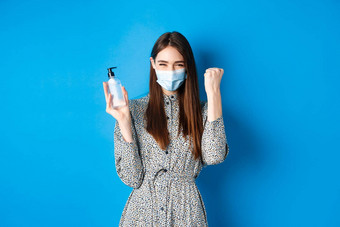 科维德社会距离医疗保健概念动机兴奋女孩医疗面具欢呼显示瓶手洗手液站蓝色的背景