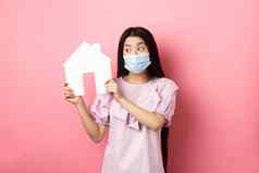 真正的房地产流感大流行概念可爱的亚洲女人医疗面具显示纸房子断路搜索财产站粉红色的背景