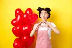 惊讶亚洲女人敬畏显示心手势使爱忏悔情人节一天站浪漫的红色的气球黄色的背景