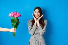 情人节一天概念兴奋快乐年轻的女人惊讶相机手拉伸手花束花接收浪漫的礼物蓝色的背景