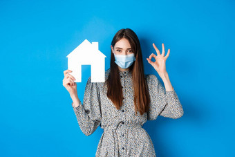 真正的房地产科维德流感大流行概念坦诚的女人医疗面具显示标志纸房子断路销售财产站蓝色的背景