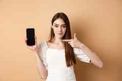自信女孩指出空智能手机屏幕显示在线促销交易站米色背景