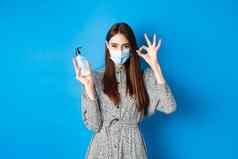 科维德社会距离医疗保健概念美丽的女孩医疗面具显示瓶防腐剂手洗手液使标志推荐产品站蓝色的背景