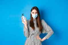 科维德社会距离医疗保健概念美丽的女孩医疗面具手消毒剂持有防腐剂瓶站蓝色的背景