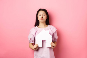 真正的房地产保险概念伤心皱着眉头亚洲女孩显示纸房子断路扮鬼脸心烦意乱站粉红色的背景
