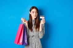 美丽的女孩购物塑料信贷卡持有纸袋购买项目站很高兴蓝色的背景