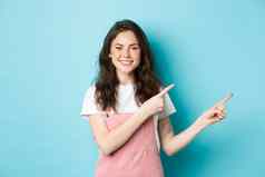 图像可爱的十几岁的女孩微笑指出手指促销提供展示横幅复制空间站夏天衣服魅力化妆蓝色的背景