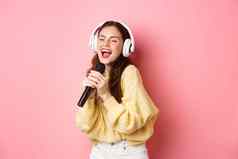 无忧无虑的女孩享受卡拉ok晚上唱歌首歌麦克风穿无线耳机站粉红色的背景