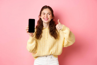 图像美丽的女人笑评级应用程序显示拇指空电话屏幕推荐在线促销站粉红色的背景