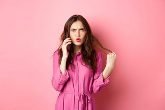 年轻的女人回答电话调用困惑优柔寡断使外卖订单智能手机站粉红色的背景