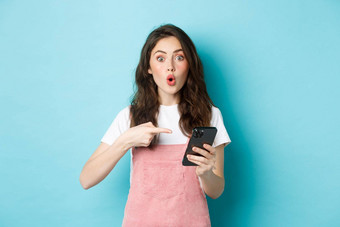 肖像兴奋女人指出手指智能手机告诉在线促销提供显示广告电话站蓝色的背景