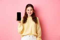技术在线购物年轻的微笑女人确定指导下载应用程序显示智能手机应用程序屏幕站粉红色的背景