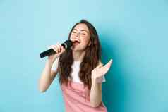 无忧无虑的美丽的女人执行首歌唱歌麦克风激情玩卡拉ok站蓝色的背景