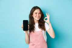 好微笑年轻的女人显示产品在线空智能手机屏幕推荐品牌使标志站满意蓝色的背景