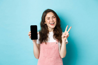 可爱的年轻的女人微笑显示地摆空智能<strong>手机</strong>屏幕<strong>演示</strong>应用程序移动商店站蓝色的背景