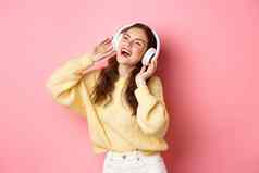 美丽的现代女孩唱歌最喜欢的首歌听音乐无线耳机微笑跳舞站粉红色的背景