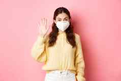 科维德封锁流感大流行概念年轻的女人穿脸面具检疫挥舞着提高了手问候人距离粉红色的背景