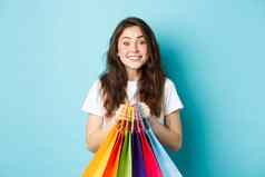 快乐的年轻的女人购买折扣持有购物袋站快乐蓝色的背景