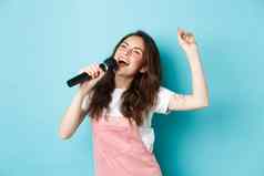 快乐年轻的女人执行首歌歌手持有麦克风跳舞唱歌卡拉ok站蓝色的背景