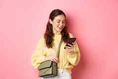 时尚的年轻的女人聊天电话站钱包阅读智能手机屏幕消息传递站粉红色的背景