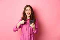年轻的女人指出手指电话微笑会说话的智能手机应用程序显示有趣的在线站粉红色的背景