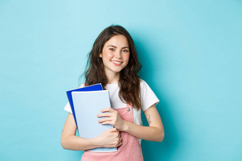 可爱的微笑女孩学生持有笔记本电脑快乐的相机研究<strong>大学大学</strong>站蓝色的背景