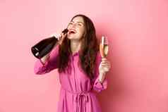 庆祝活动假期概念快乐无忧无虑的女人喝香槟瓶很高兴微笑放松聚会，派对持有玻璃站粉红色的背景