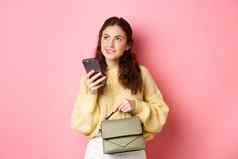 图像美丽的女模型持有钱包智能手机深思熟虑的思考回答消息站粉红色的背景