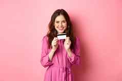 美丽的年轻的女人显示塑料信贷卡微笑购物商店站粉红色的背景