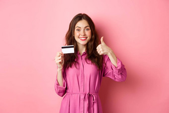 浅黑肤色的女人女孩显示拇指微笑推荐银行持有塑料信贷卡站粉红色的背景